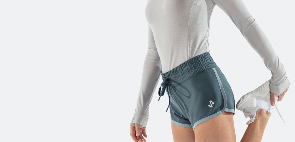 Woman stretching in Tempo drawstring shorts showing Tempo logo on left leg